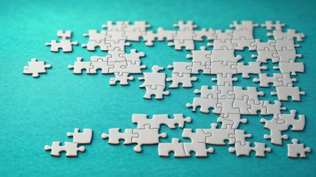 White jigsaw puzzle pieces arranged on turquoise felt with soft shadows and visible gaps.