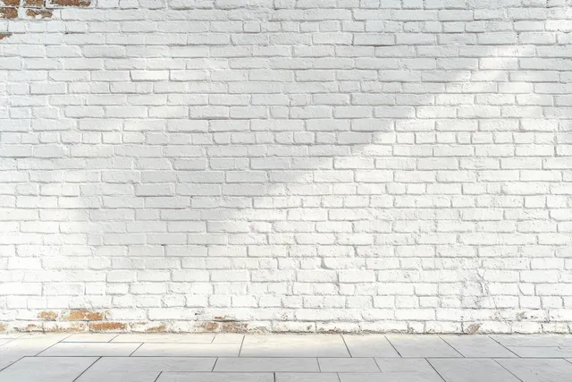 White brick wall with faint shadow lines above a smooth gray tiled floor in an empty room.