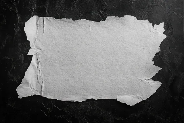 Una hoja de papel blanco en blanco, rasgada y arrugada, yace plana sobre una superficie negra texturizada con bordes ásperos.