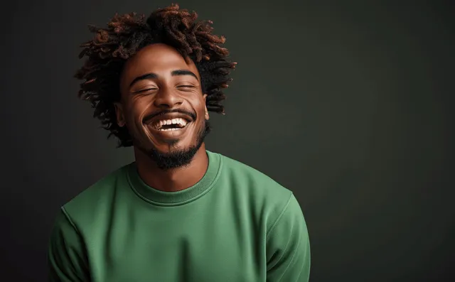 Young man in a green sweatshirt laughing in front of a dark studio background.
