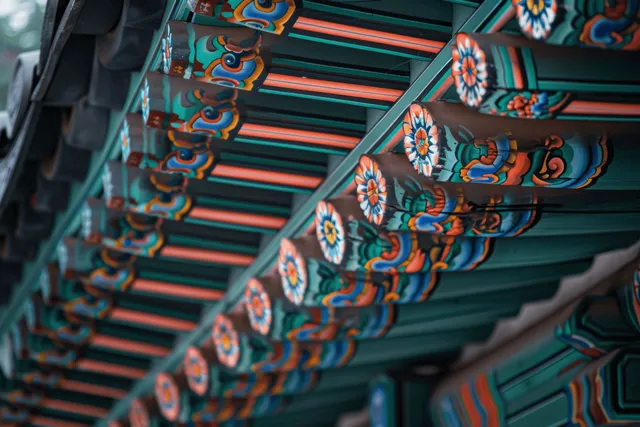 Close-up of colorful painted Korean wooden roof brackets under eaves with ornate repeating patterns.