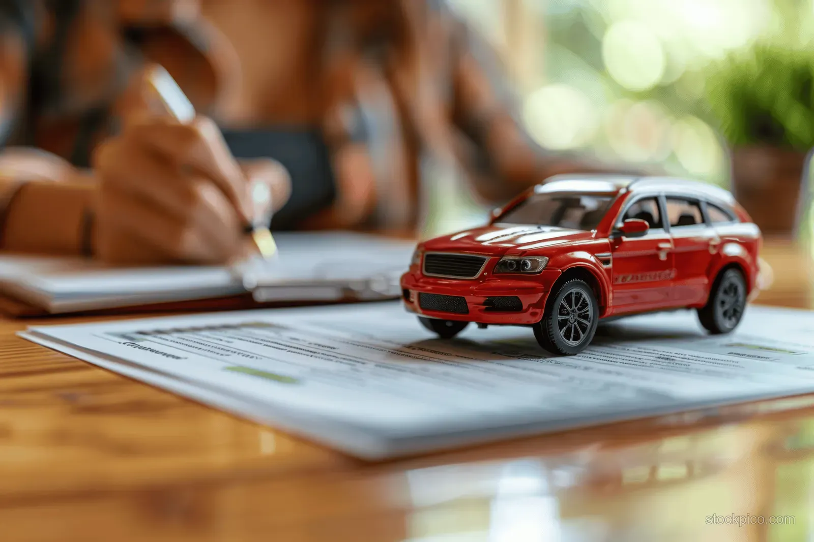 A woman’s hand signs an auto contract while a red model car rests on the signed documents.